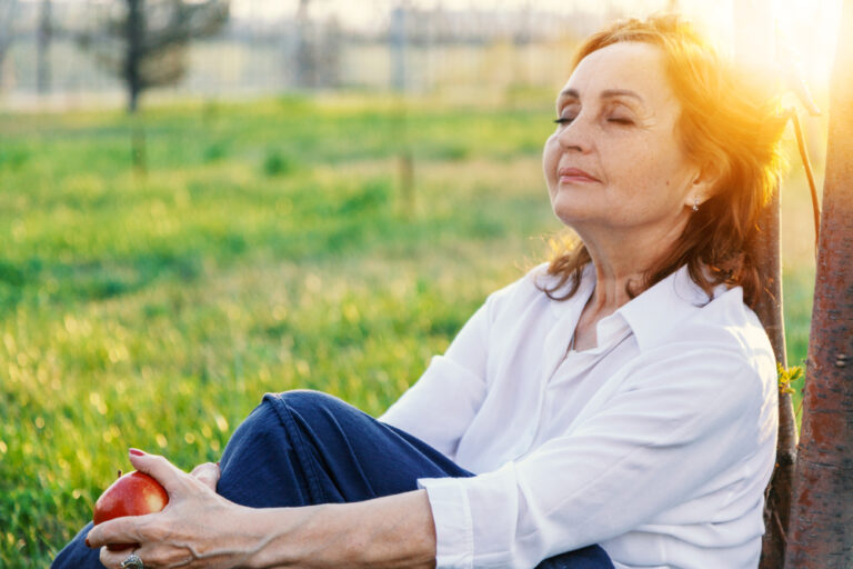 Happy,Senior,Woman,Relaxing,On,Green,Lawn